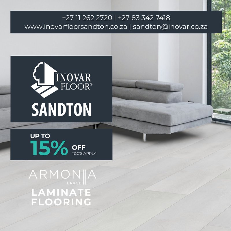 A minimalist, contemporary living room with a large grey sectional sofa, showcasing the clean, expansive look of Armonia Large laminate flooring in a bright, cool-toned finish.